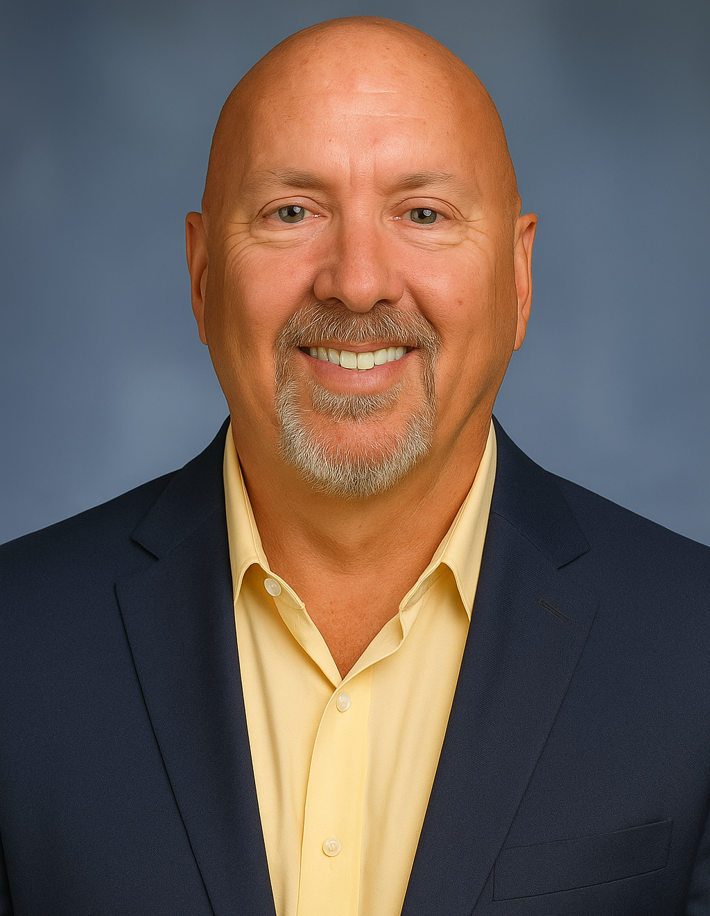 Business Leadership Portrait — JAC Consulting Smiling professional man in a navy blazer and yellow shirt, photographed against a soft blue background for JAC Consulting branding.